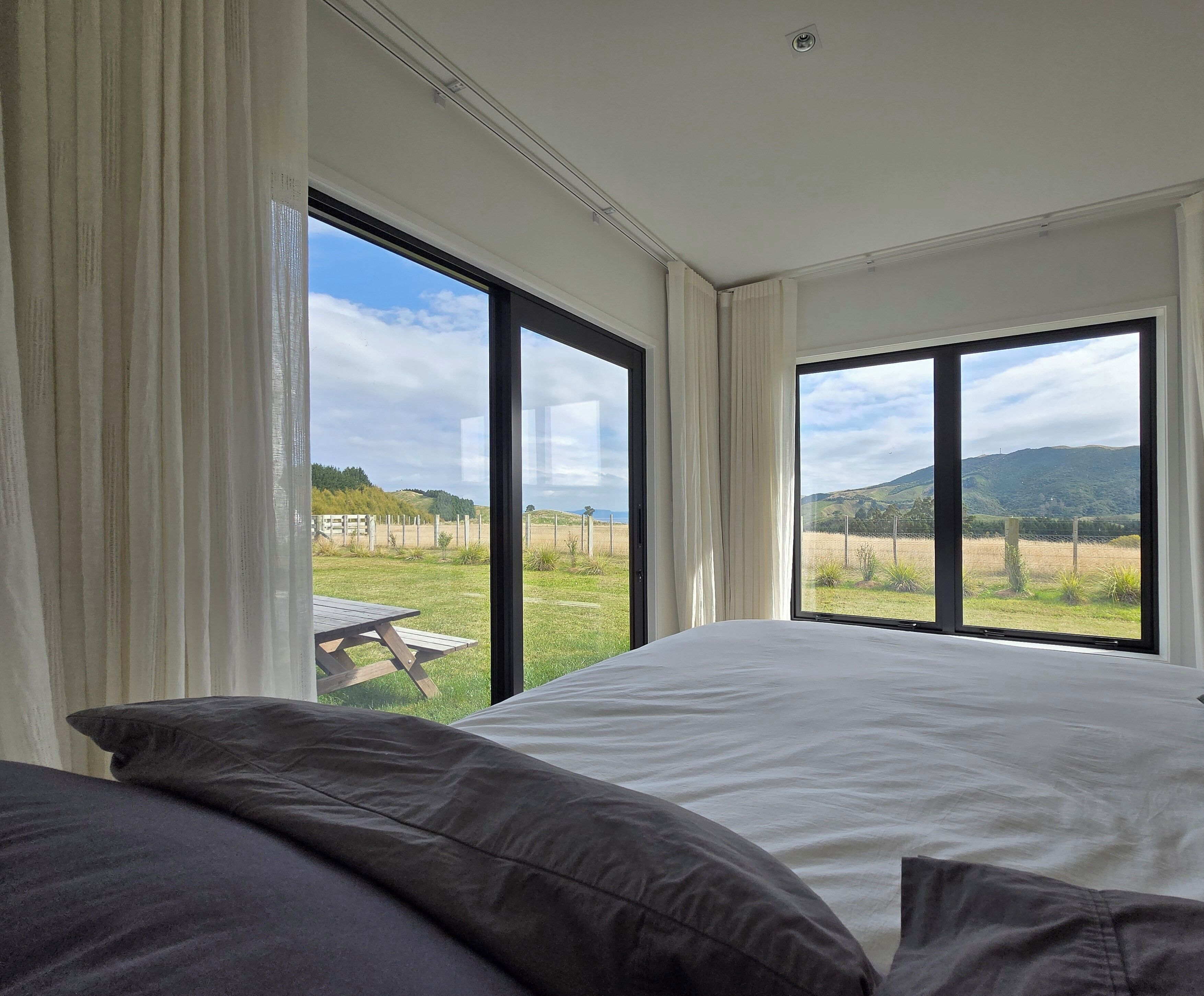 A bedroom with a large bed, two windows, and a view of a grassy field.