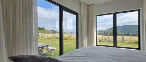 A bedroom with a large bed, two windows, and a view of a grassy field.