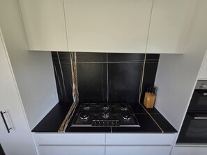 Eine Küche mit schwarzem Fliesenrückwand, einem Gasherd und weißen Schränken.