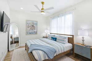 A bedroom with a bed, bedside tables, a ceiling fan, a mirror, and a painting. - IRB Coastal Escape, 5BR All En-Suite, Pool & Dock (Indian Rocks Beach)