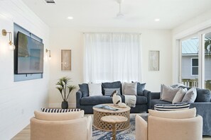 A modern living room with a grey sofa set, a round coffee table, and a large flat-screen TV mounted on the wall. - IRB Coastal Escape, 5BR All En-Suite, Pool & Dock (Indian Rocks Beach)
