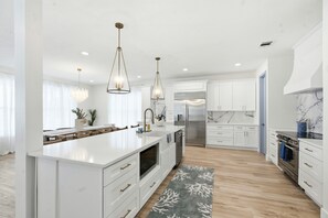 A modern kitchen with white cabinetry, a central island, stainless steel appliances, and pendant lighting. - IRB Coastal Escape, 5BR All En-Suite, Pool & Dock (Indian Rocks Beach)