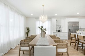 Une cuisine moderne avec des meubles blancs, un réfrigérateur en acier inoxydable et un coin repas comprenant une table en bois et des chaises en osier.