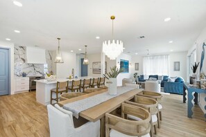 A spacious living area with a long wooden dining table, multiple chairs, and a chandelier. - IRB Coastal Escape, 5BR All En-Suite, Pool & Dock (Indian Rocks Beach)