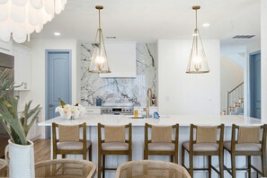 Une cuisine moderne avec un revêtement mural en marbre, un îlot central doté de tabourets et un éclairage suspendu.