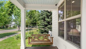 A porch with a wooden swing, a white exterior wall, and a view of a residential street. - Northern Charm with 3BDR & Game Room (Kalispell)