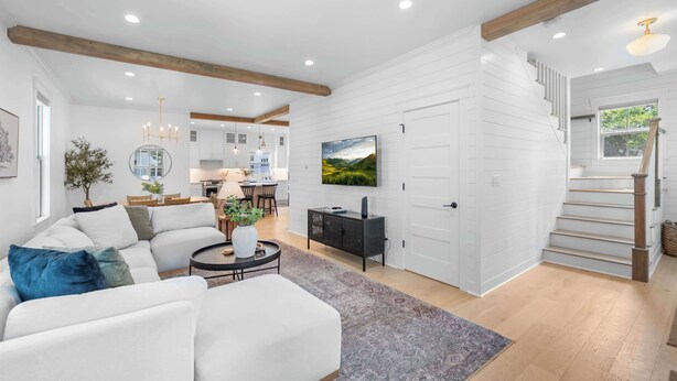 A modern living room with a sectional sofa, a dining area, a kitchen, and a staircase leading to another level. - Northern Charm with 3BDR & Game Room (Kalispell)