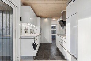 A modern kitchen with white cabinetry, a stainless steel sink, and a black oven mitt hanging on the door handle. - Cosy holiday home near Kerteminde (Kerteminde)