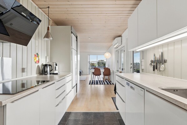 A modern kitchen with white cabinetry, a black range hood, and a dining area with a view.