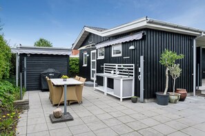 A patio area with a table and chairs, a grill, and a small garden with potted plants.