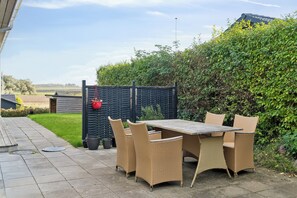 An outdoor patio with a table and chairs, a black fence, and a hedge. - Cosy holiday home near Kerteminde (Kerteminde)
