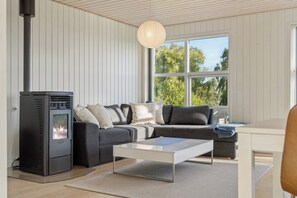 A modern living room with a fireplace, a sofa set, a coffee table, and a large window with a view of trees. - Cosy holiday home near Kerteminde (Kerteminde)