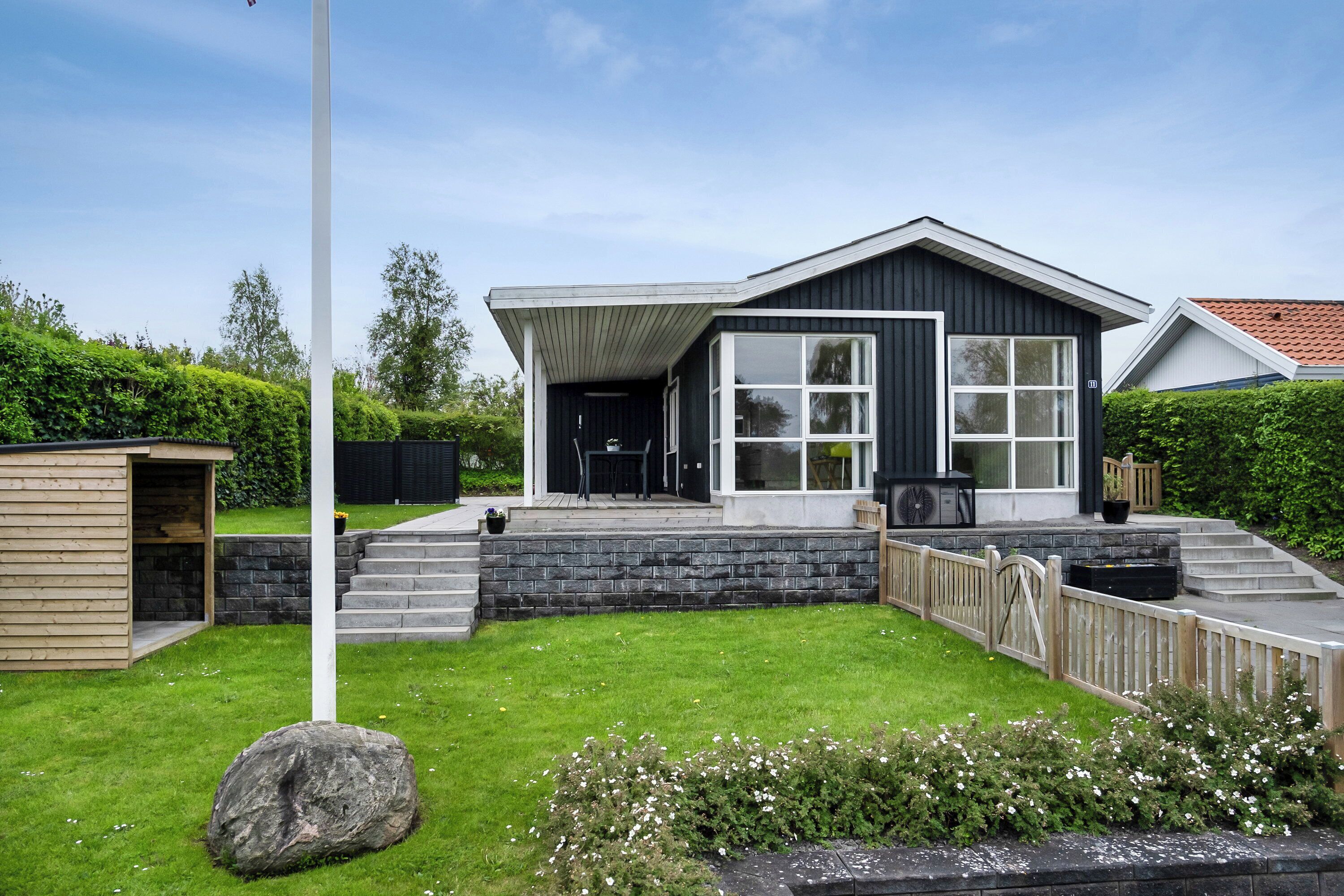 Et moderne hus med en stor veranda, en støttemur af sten og et flagstang.
