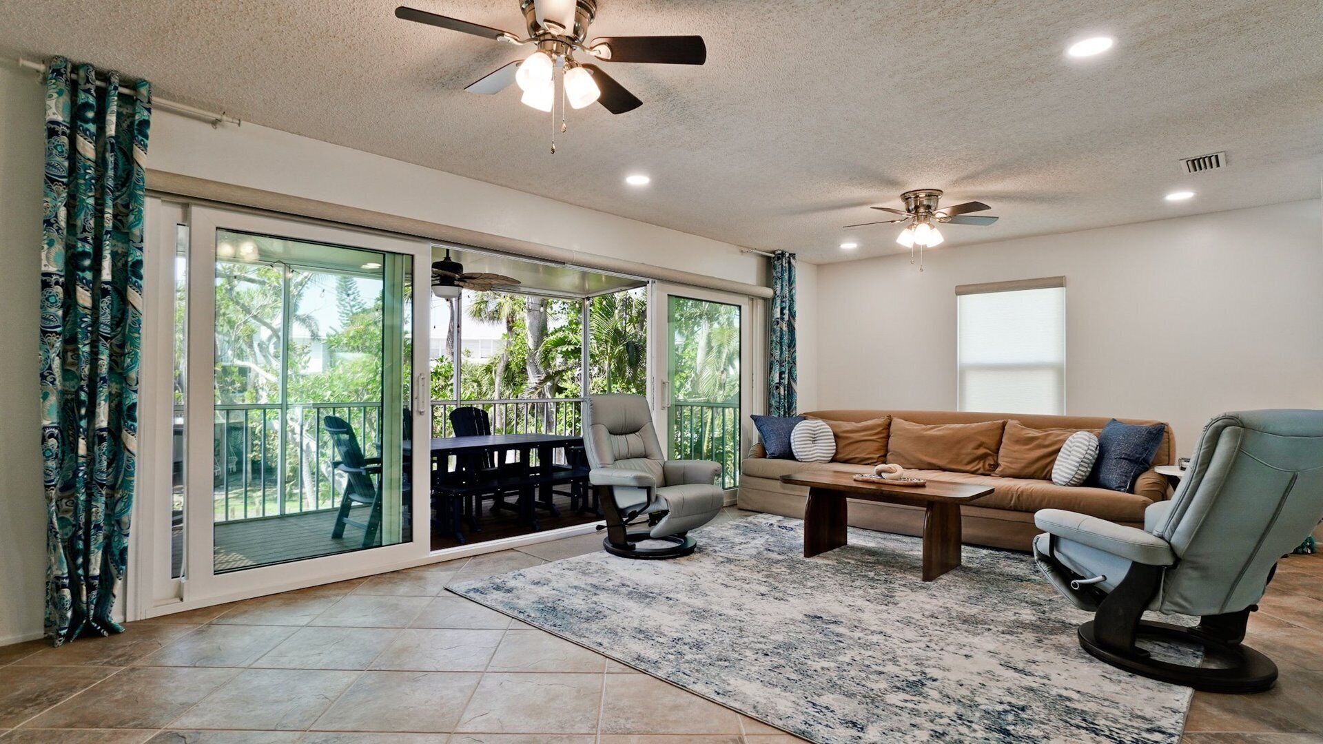 A spacious living area with a sliding glass door leading to a balcony, a sofa, a coffee table, and two chairs.