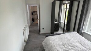 Un dormitorio con una cama, un ventilador de techo, una ventana con cortinas y vista a la cocina.