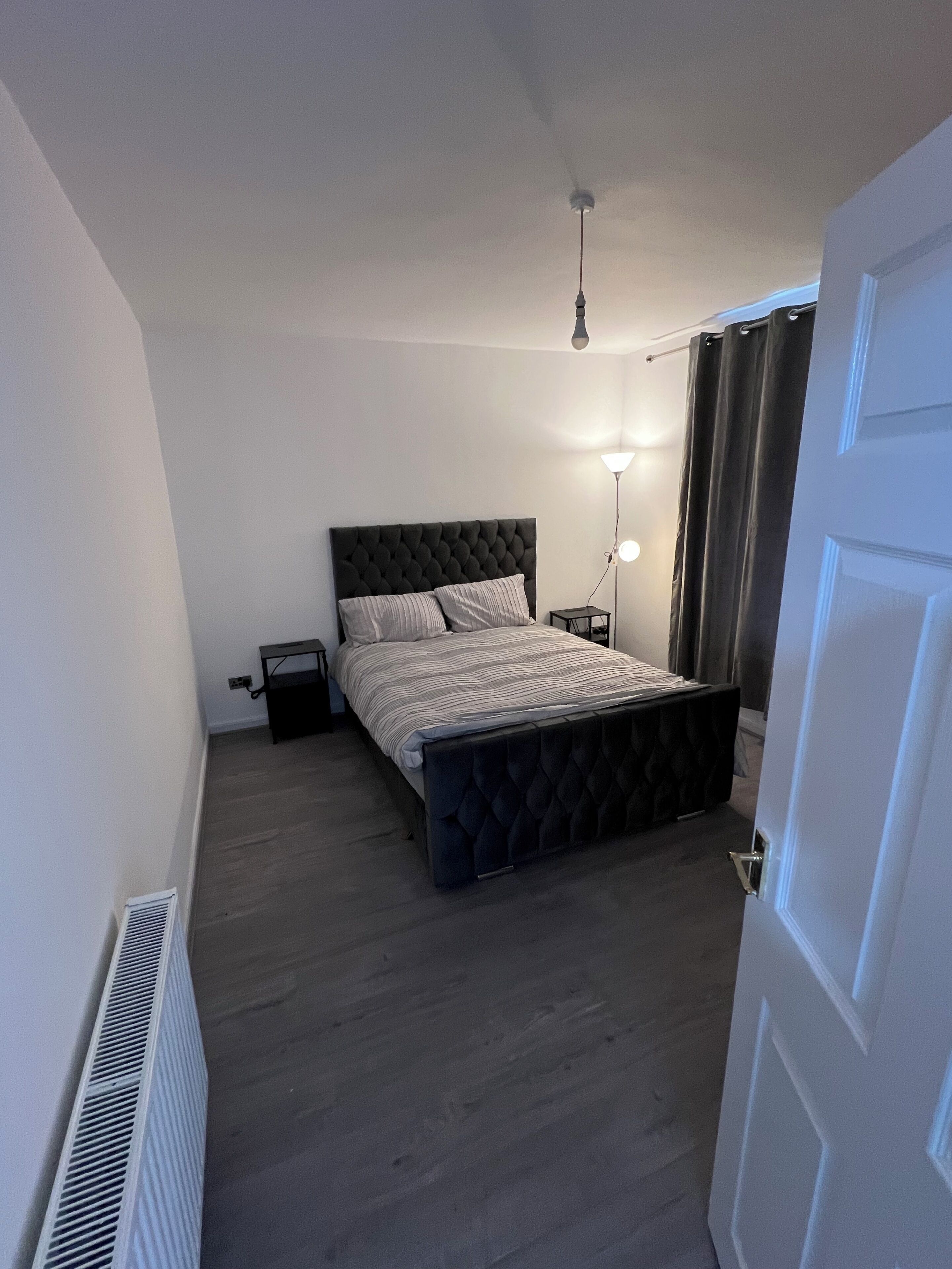Un dormitorio con cama, mesitas de noche, una lámpara y una puerta.
