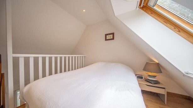 A bedroom with a sloped ceiling, a bed, a bedside table with a lamp, and a small picture frame on the wall. - Votre cocon breton • Calme & Jardin (Quéven)