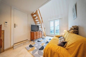 A room with a bed, a TV, a staircase, and a window. - Votre cocon breton • Calme & Jardin (Quéven)