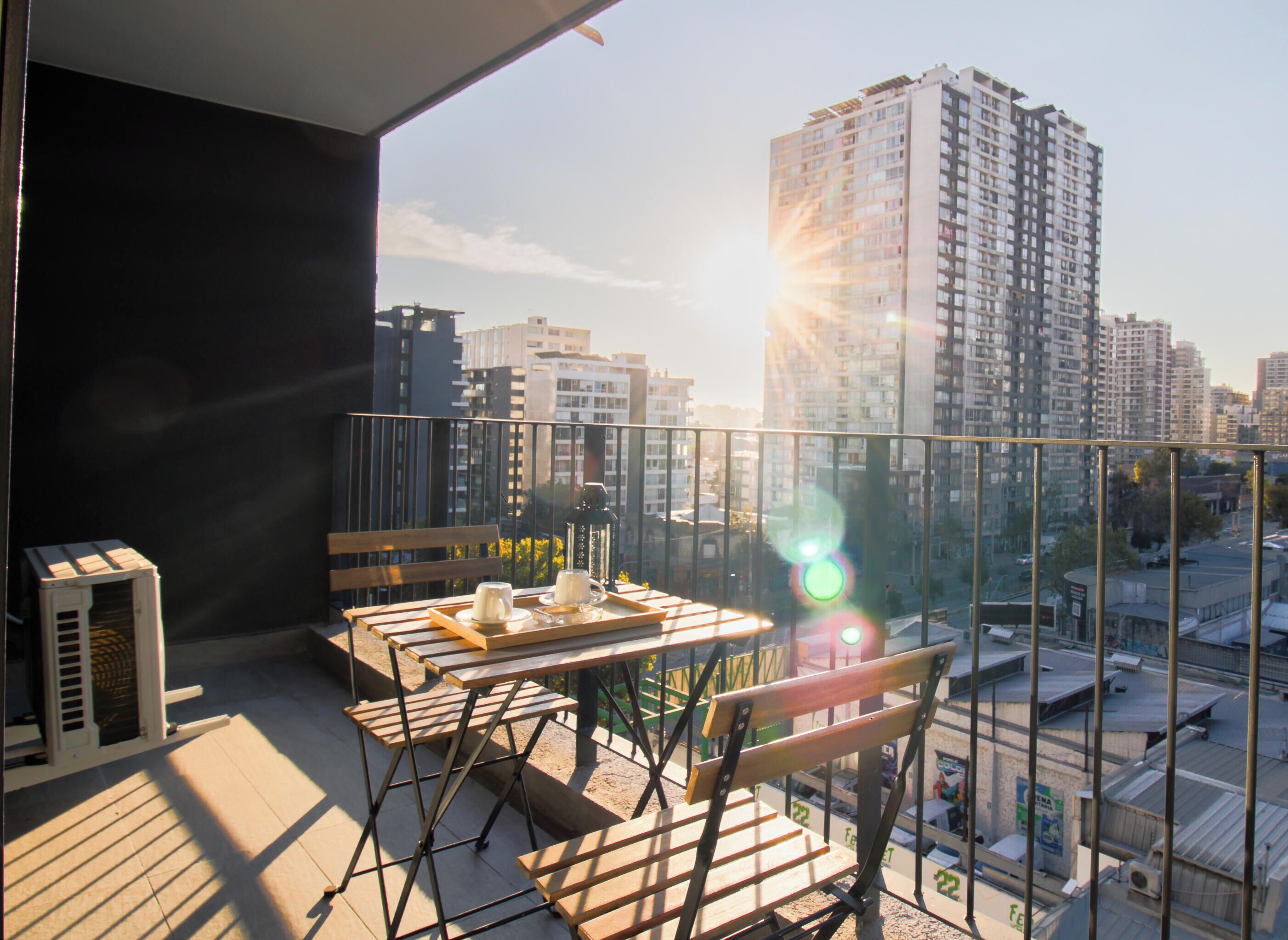 A balcony with a table and chairs, overlooking a cityscape with high-rise buildings.