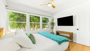 Une chambre à coucher avec un lit, une télévision, un ventilateur de plafond et de grandes fenêtres.