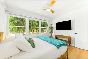 A bedroom with a bed, a TV, a ceiling fan, and large windows. - The Tourmaline Beach House - Walk to Surf & Sand (San Diego)