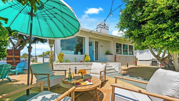 Un espace patio aménagé avec du mobilier d’extérieur, une table dressée avec de la nourriture et des boissons, et un grand parasol offrant de l’ombre.