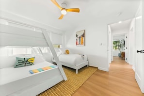 A modern, well-lit room with a bed, a ceiling fan, and a painting of surfboards. - The Tourmaline Beach House - Walk to Surf & Sand (San Diego)
