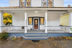 A two-story house with a porch, a front door with a glass panel, and a mailbox. - Beautiful 1910 Home | Jetted Tub | DT Wallace (Wallace)
