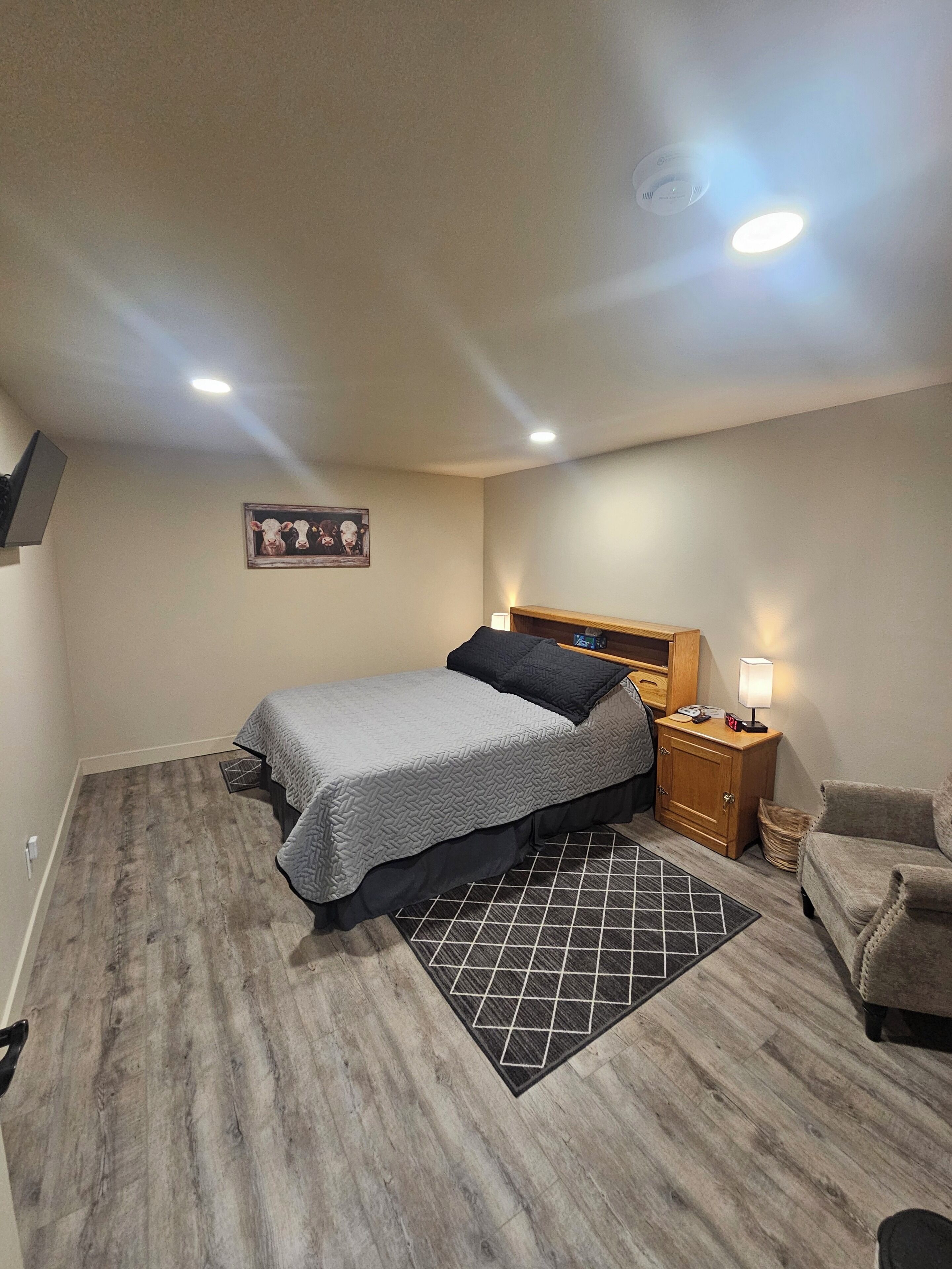 A bedroom with a bed, a nightstand, a lamp, a chair, and a picture on the wall.