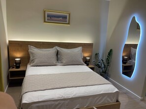 A modern bedroom with a wooden headboard, a large bed with white bedding, two bedside lamps, and a framed picture on the wall.