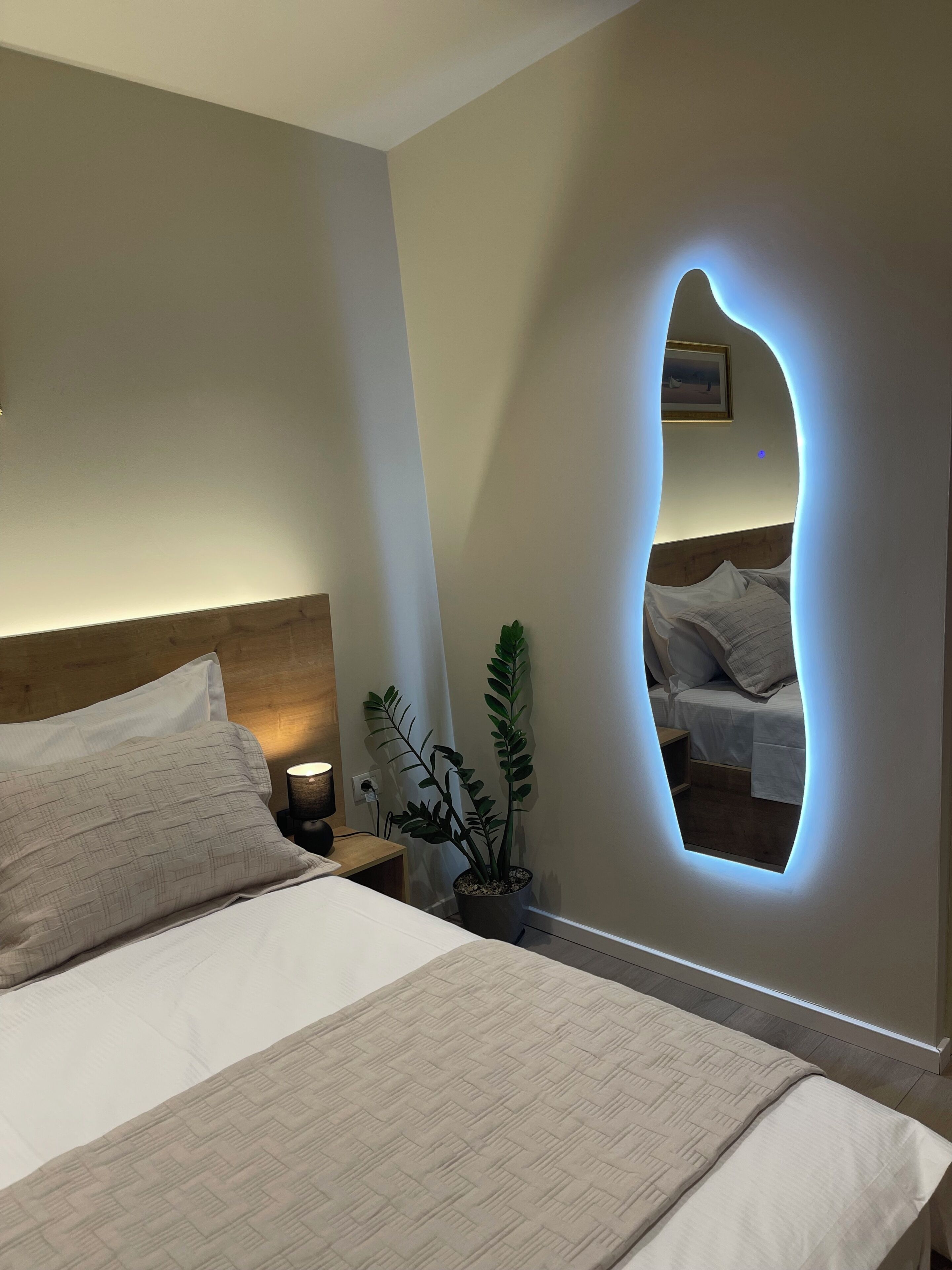 Un dormitorio con cama, mesita de noche, lámpara y una planta en maceta.