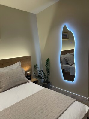 A bedroom with a bed, bedside table, lamp, and a potted plant.