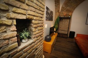A room with exposed brick walls, a fireplace, a wooden bench, and a red sofa. - Loft con Archi Romani | Cuore di Trastevere (Rome)