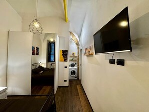 A narrow hallway with a flat-screen TV mounted on the wall, a washing machine, and a bed with a headboard. - Loft con Archi Romani | Cuore di Trastevere (Rome)