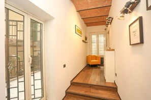 A hallway with a wooden staircase, a yellow sofa, and a door leading to a balcony. - Loft con Archi Romani | Cuore di Trastevere (Rome)