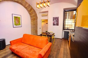 A cozy room with a sofa, a dining table, and chairs. There's a kitchen area with a stove and a radiator. - Loft con Archi Romani | Cuore di Trastevere (Rome)