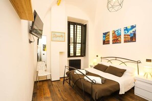 A bedroom with a bed, a chair, a TV mounted on the wall, and three paintings on the wall. - Loft con Archi Romani | Cuore di Trastevere (Rome)