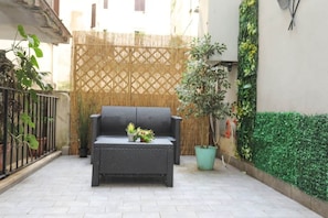 A patio with a woven fence, a black wicker sofa, and potted plants. - Loft con Archi Romani | Cuore di Trastevere (Rome)