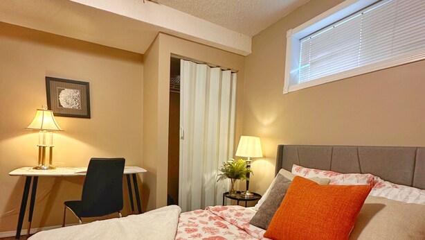 A hotel room with a bed, a desk, a chair, a window, and a door.