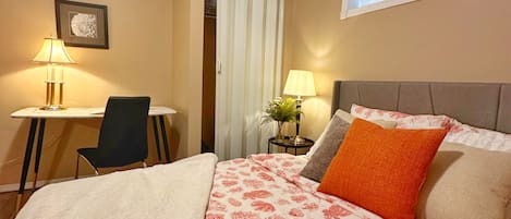 A hotel room with a bed, a desk, a chair, a window, and a door.