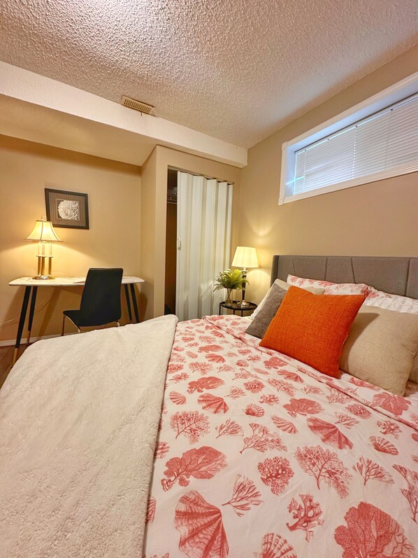 A hotel room with a bed, a desk, a chair, a window, and a door.