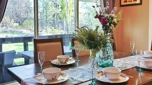 A dining area with a table set for four, a vase with flowers, and a view of the outdoors.