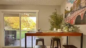 A dining area with a table and stools, a sliding glass door leading to a patio, and a mural on the wall.