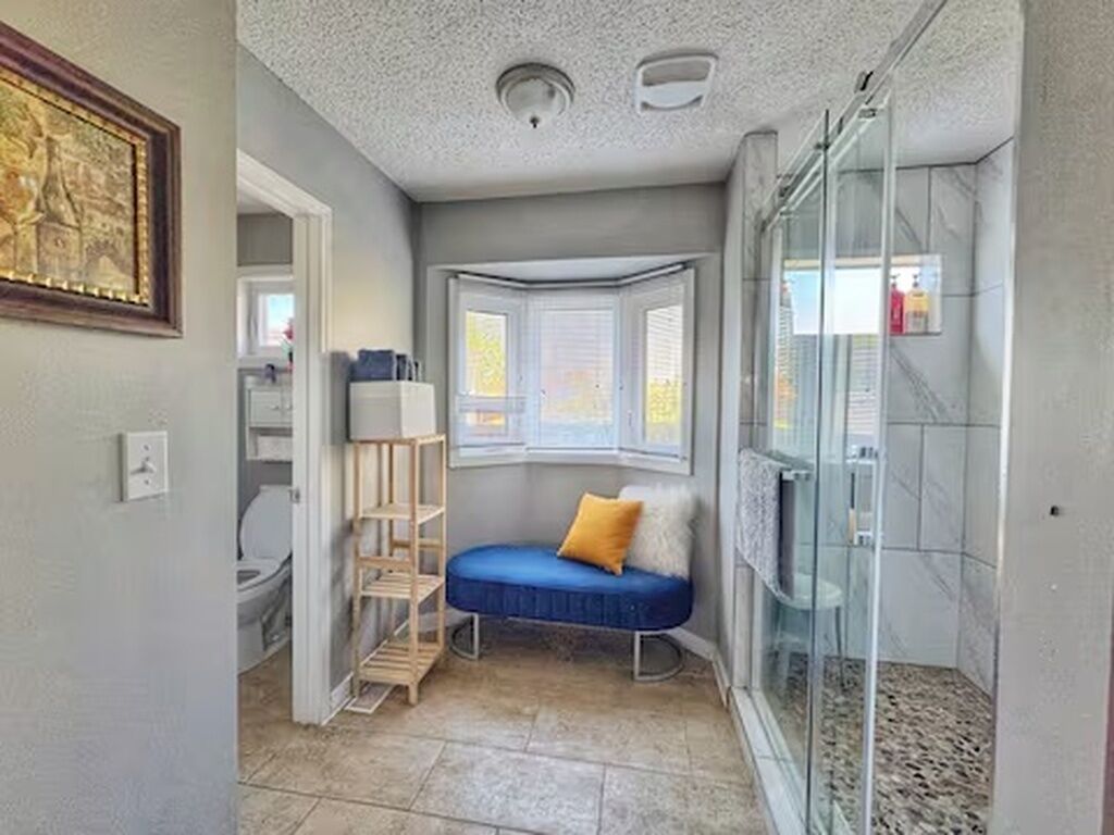 Ein Badezimmer mit Dusche, einem Fenster und einer Sitzbank.