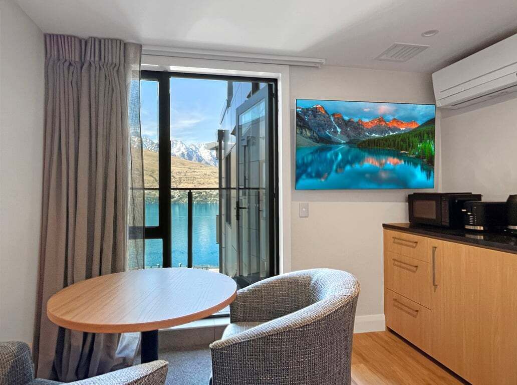 A modern room with a dining table, chairs, a kitchen area, and a large window with a mountain view.