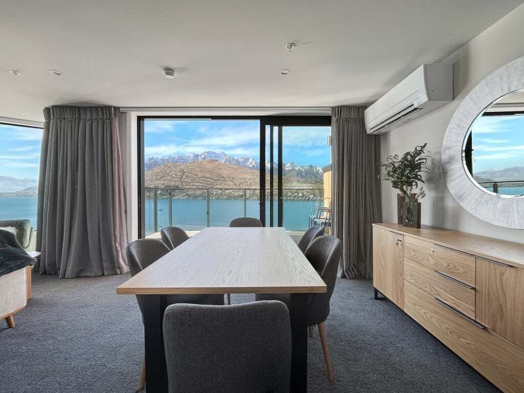 Une chambre d’hôtel moderne dotée d’une grande table à manger, de sièges confortables, d’une vue sur les montagnes et d’un balcon.