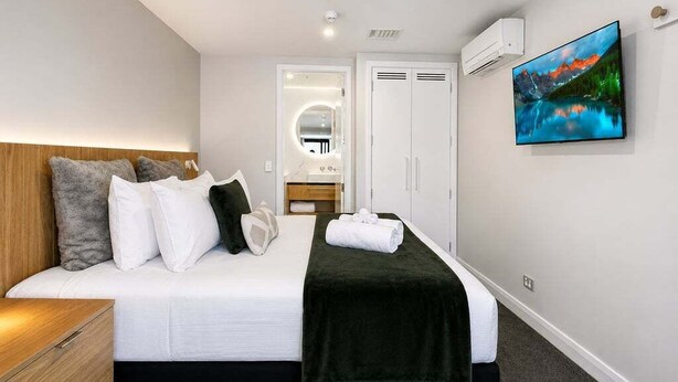 Habitación de hotel con cama, cabecero de madera, televisor de pantalla plana, espejo y armario.