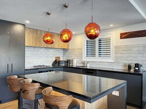 A modern kitchen with a large island, pendant lighting, and wooden bar stools. - Above the Lake | Queenstown Sanctuary (Queenstown)