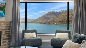 Una habitación con un ventanal grande que ofrece vistas a la montaña, dos sillones con almohadones suaves, una mesa de centro de cristal y un cuadro en la pared.