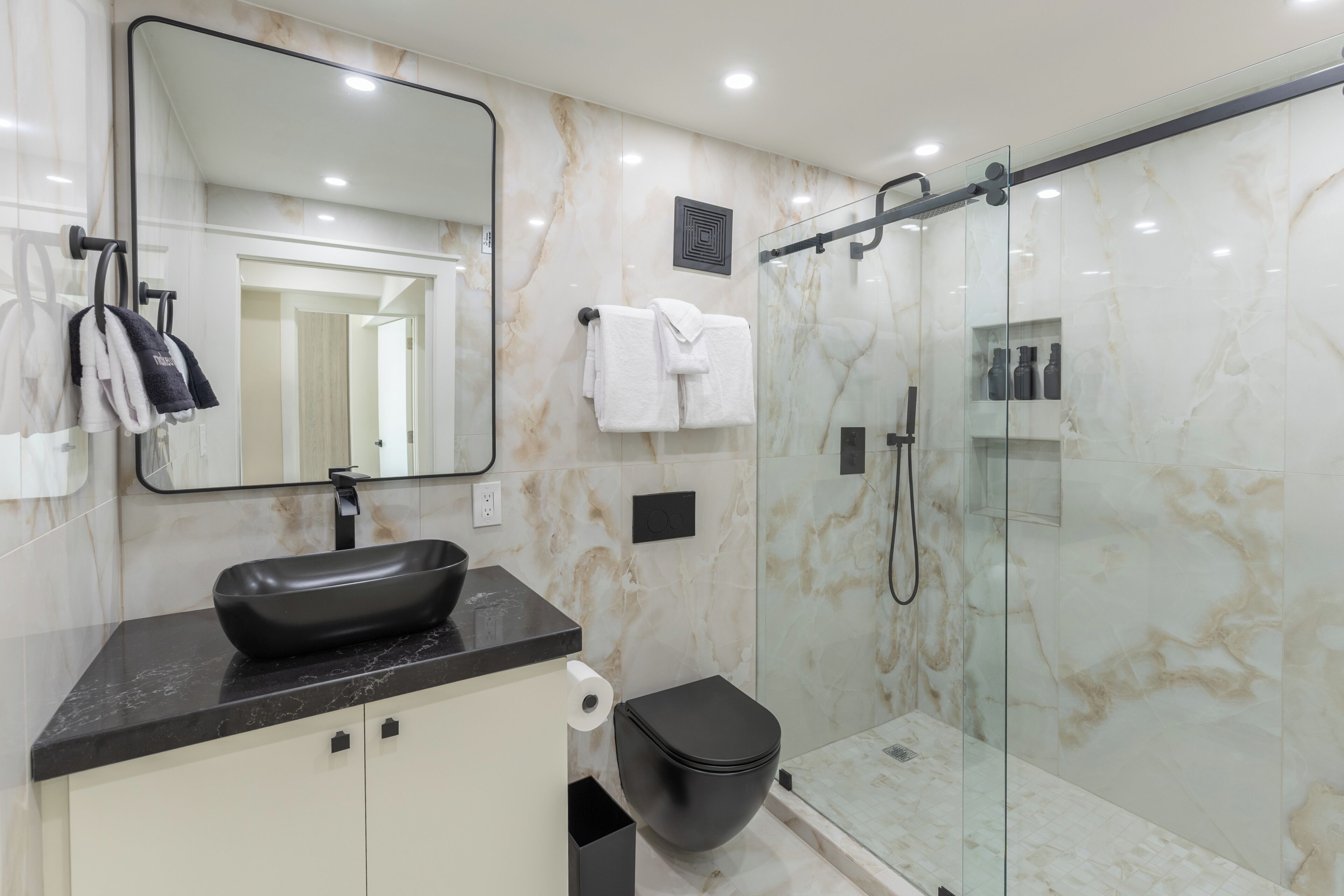 A modern bathroom with a black vessel sink, a glass-enclosed shower, and a toilet.